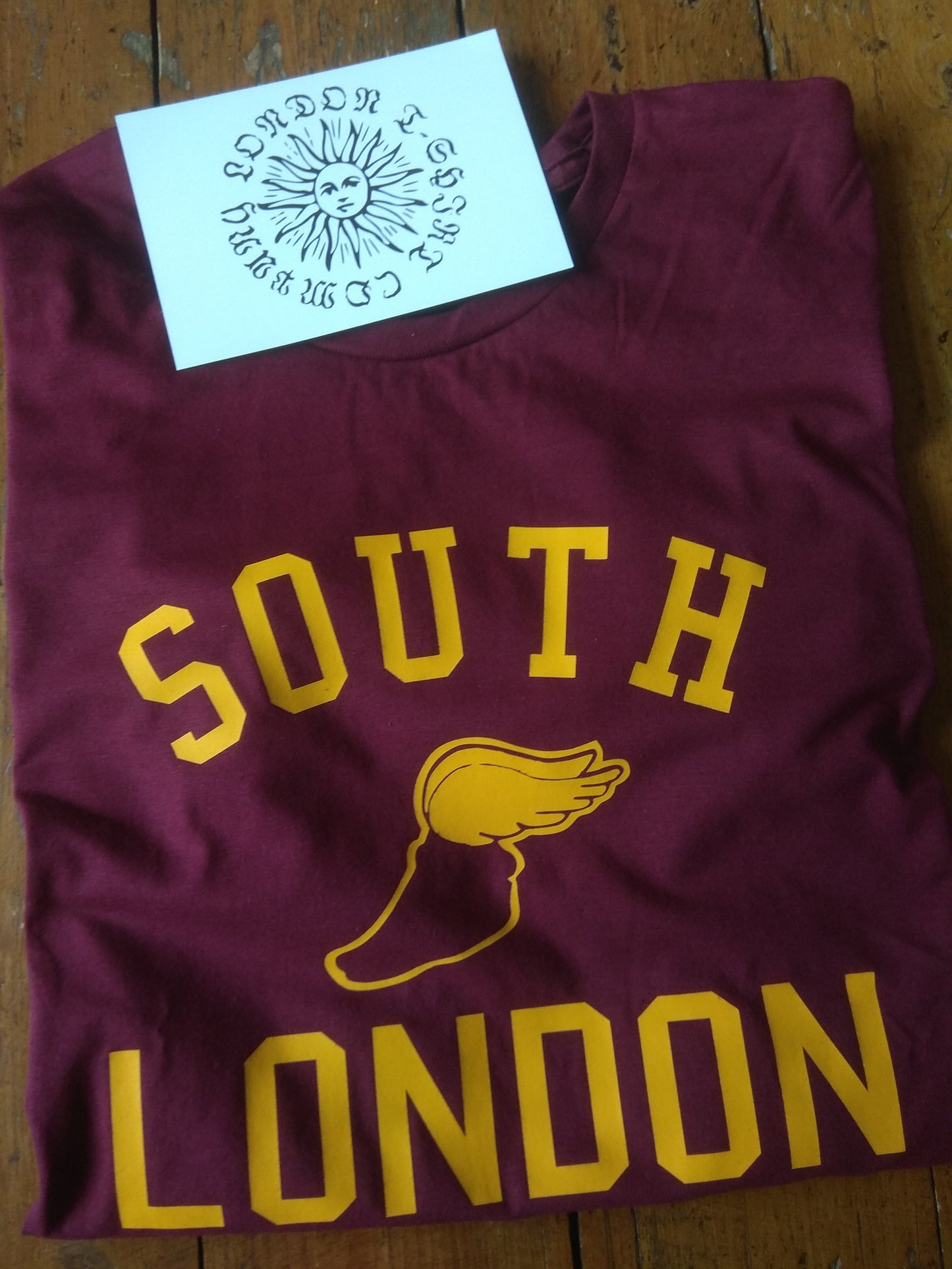 Maroon t-shirt with 'South London' text and logo on a wooden surface